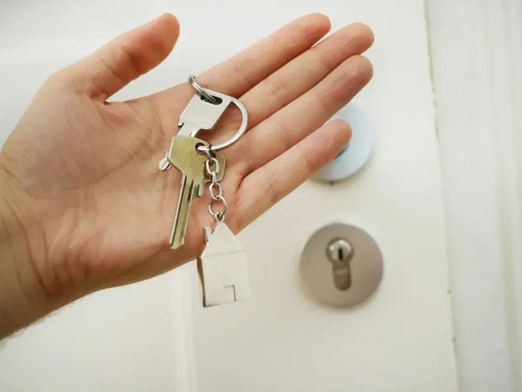 Hand holding house keys in front of a locked door